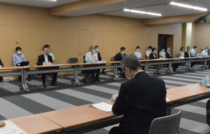 写真:長机が横にくっついて並べられ、間隔をあけて出席者が席についている。向かい合うように同じような席が作られている。