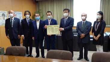 写真:表彰状を共に手にして並ぶ、鈴木浜松市長と衛藤大臣。二人を挟んで5人の浜松市職員が並んでいる。全員がマスクをしている。