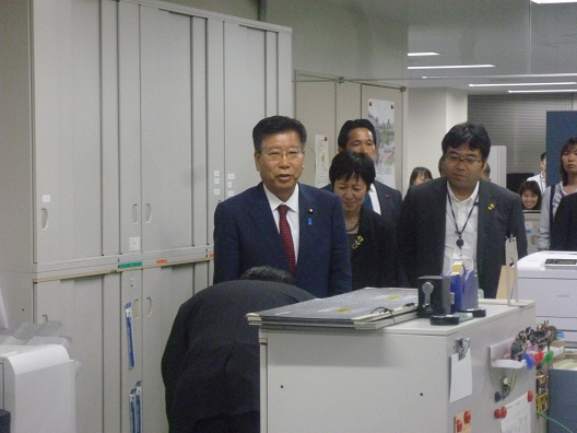 写真:棚が並ぶ執務室の通路を案内される衛藤大臣。