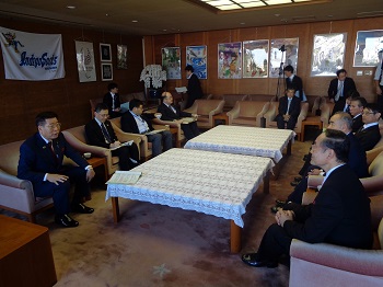 写真:広いテーブルを囲むように、一人掛けのソファが10個余り配置されている部屋。10人ほどが席に付き懇談している。写真左の手前側に座り、話をしている衛藤大臣。