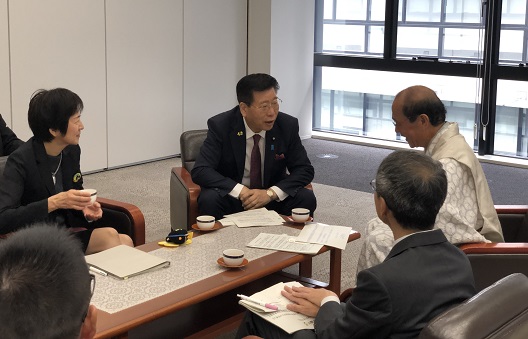 写真:膝の高さまでの小さなテーブルを囲むようにして、4、5人がそれぞれ、小さなソファに座っている。写真正面に衛藤大臣が座り、斜めに向かい合うように門川京都市長が座っている。