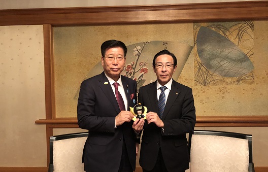 写真:衛藤大臣と西脇京都府知事が、共にてのひらサイズの「イヤヤン」のぬいぐるみに手をかけ、並んで立っている。