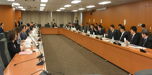 写真:机が大きくコの字型に配置された部屋。20人強が席についている。