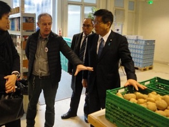 写真:団体職員より説明を受けいている衛藤大臣。横には、コンテナの中に入った野菜が置いてある。