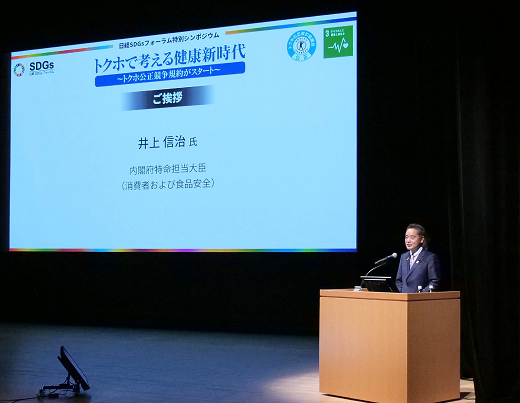 写真:大きなスクリーンの前におかれた演台に立って挨拶している井上大臣