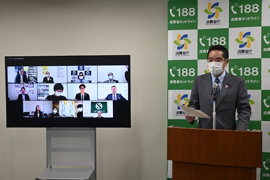 写真:右側、演台の前で祝辞を述べる井上大臣。左のテレビモニターでは、複数の受賞者が並んでいる。