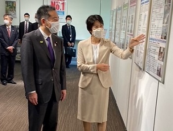 写真:壁に貼られた資料を見ながら、職員より説明を受ける井上大臣