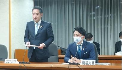 写真:横長の会議机、右側には、小泉環境大臣が座り、左側では、井上大臣が立ち上がって話をしている。