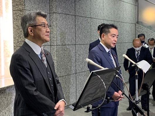 写真:画面左には、手を組んで立っている総務大臣。その右側に、井上大臣が並び、取材に応じ話をしている