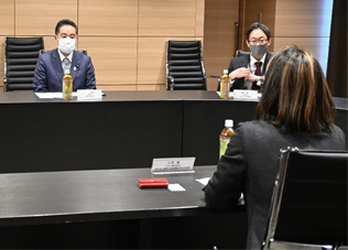 写真:丸く並べられた机の席につく井上大臣。向かい合うようにして参加者が座っている