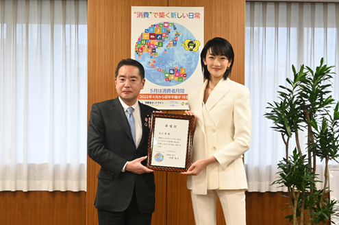 写真:井上大臣と冨永愛氏が、「エシカルライフスタイルSDGsアンバサダー」の委任状を間に持ち、並んで立っている。