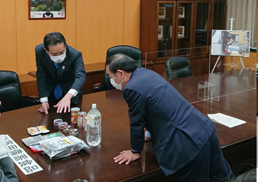 写真:机の上に置かれた災害用備蓄品を見ながら、話をする井上大臣と坂本大臣