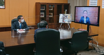 写真:部屋の奥に置かれたモニターに、古谷代理理事が移っている。席に付き、モニターを見る井上大臣と坂本大臣