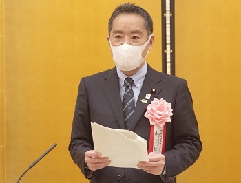 写真:祝辞を読む井上大臣。胸には、ピンクの花の記章を着けている