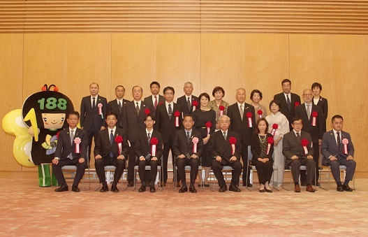 写真:受賞者30人弱が前後に列に並び、記念撮影。前列の真ん中に、井上大臣が座っている。後列の左横には、イヤヤンの着ぐるみが立っている。