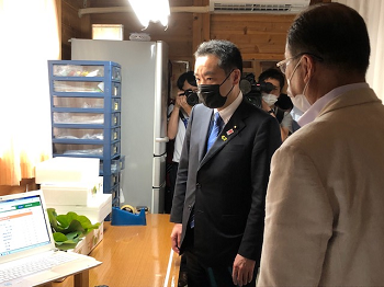 写真:作業室、パソコンの置かれた一角で、説明を受けている井上大臣。