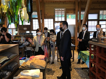 写真:ゼロウェイトセンター内、衣料の置かれた棚の前に立ち、職員より取組説明を受けている井上大臣。