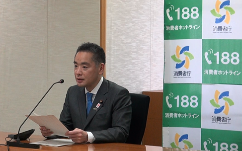 写真:消費者庁のロゴマークの並んだバックスクリーンの前に座り、発言している井上大臣。