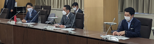 写真:写真左から、環境省の小泉大臣、消費者庁の井上大臣、経済産業省の佐藤政務官が並んで座っている。会議机のそれぞれの間には、透明のパーテーションが立てられている。参加者はみなマスクを着けている。