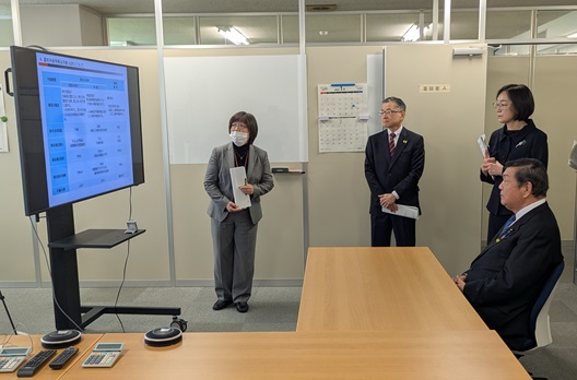 写真:モニターを前にして職員から説明を受けている伊東大臣