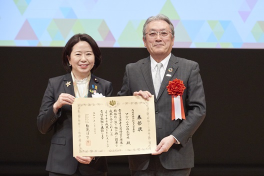 写真:自見大臣と受賞者が、表彰状を間に掲げ持ち並んでいる。