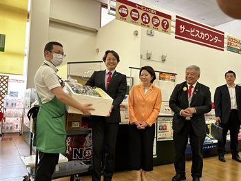 写真:食品の入った箱が手渡されるところを見ている自見大臣