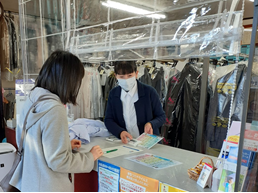 Photo: Dry-cleaned clothes are lined up in the store, and an employee is showing a magnet with a quick laundry label to a customer and explaining it to them.