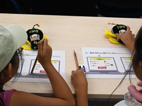 写真:子どもたちが、職員の説明を聞きながらクイズに書き込んでいる様子