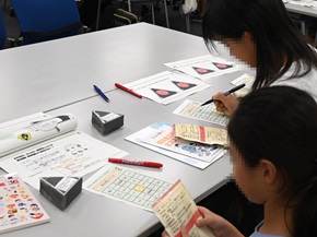 写真:子どもたちが、職員の説明を聞きながらクイズに書き込んでいる様子