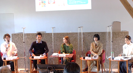 写真:一人掛けのソファと机のセットが5つ並び、5人の男女が座っている。それぞれの間は、透明のパーテーションで区切られている。