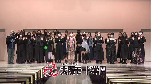 写真:30人弱が舞台の上に並んでいる集合写真。