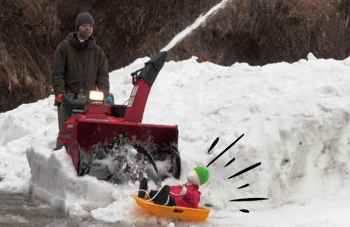 写真:除雪機を操作し除雪中の男性と、その死角からソリで子ども(ダミー人形)が滑ってきている